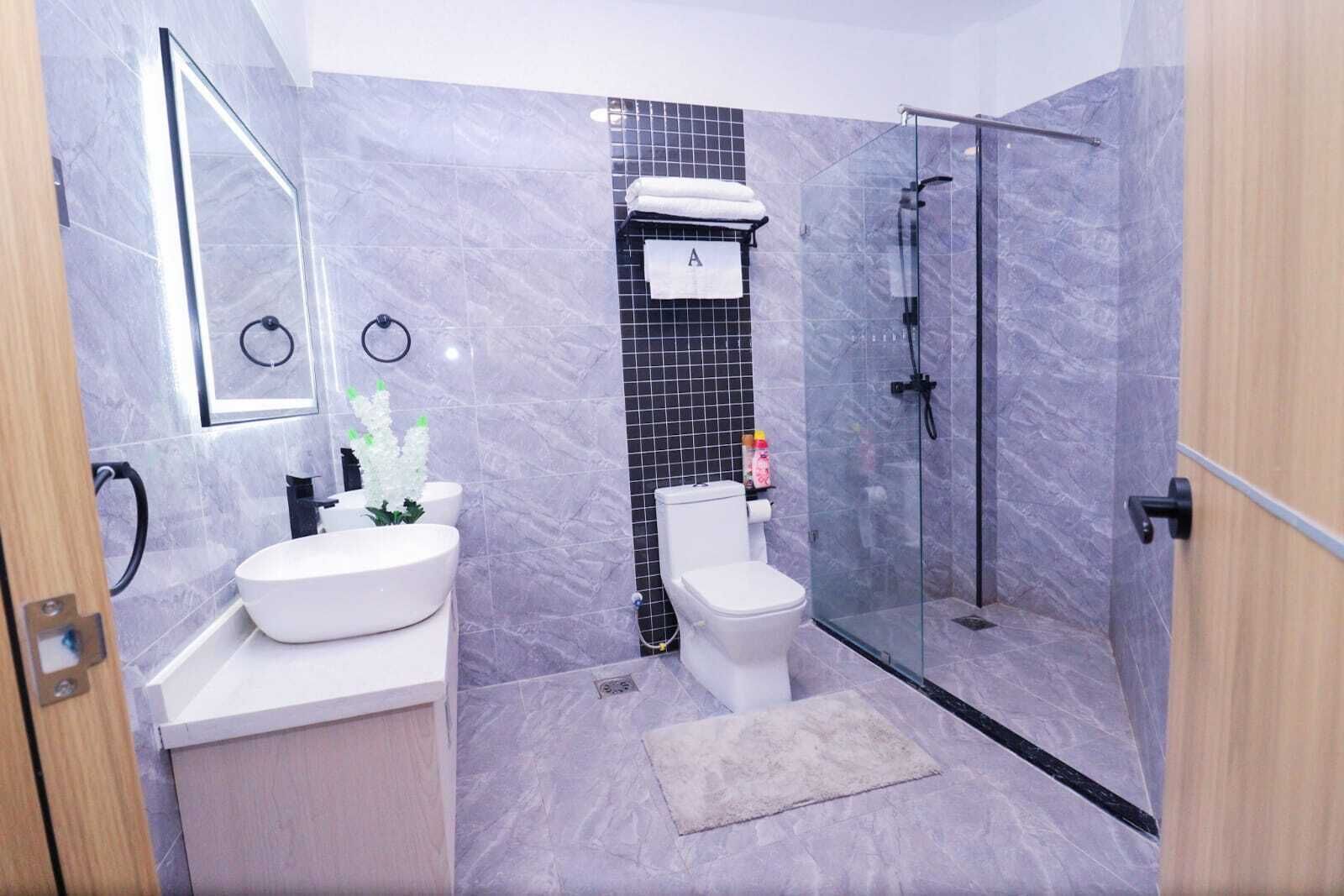A modern bathroom with a marble floor, a white sink, a toilet, and a glass-enclosed shower.