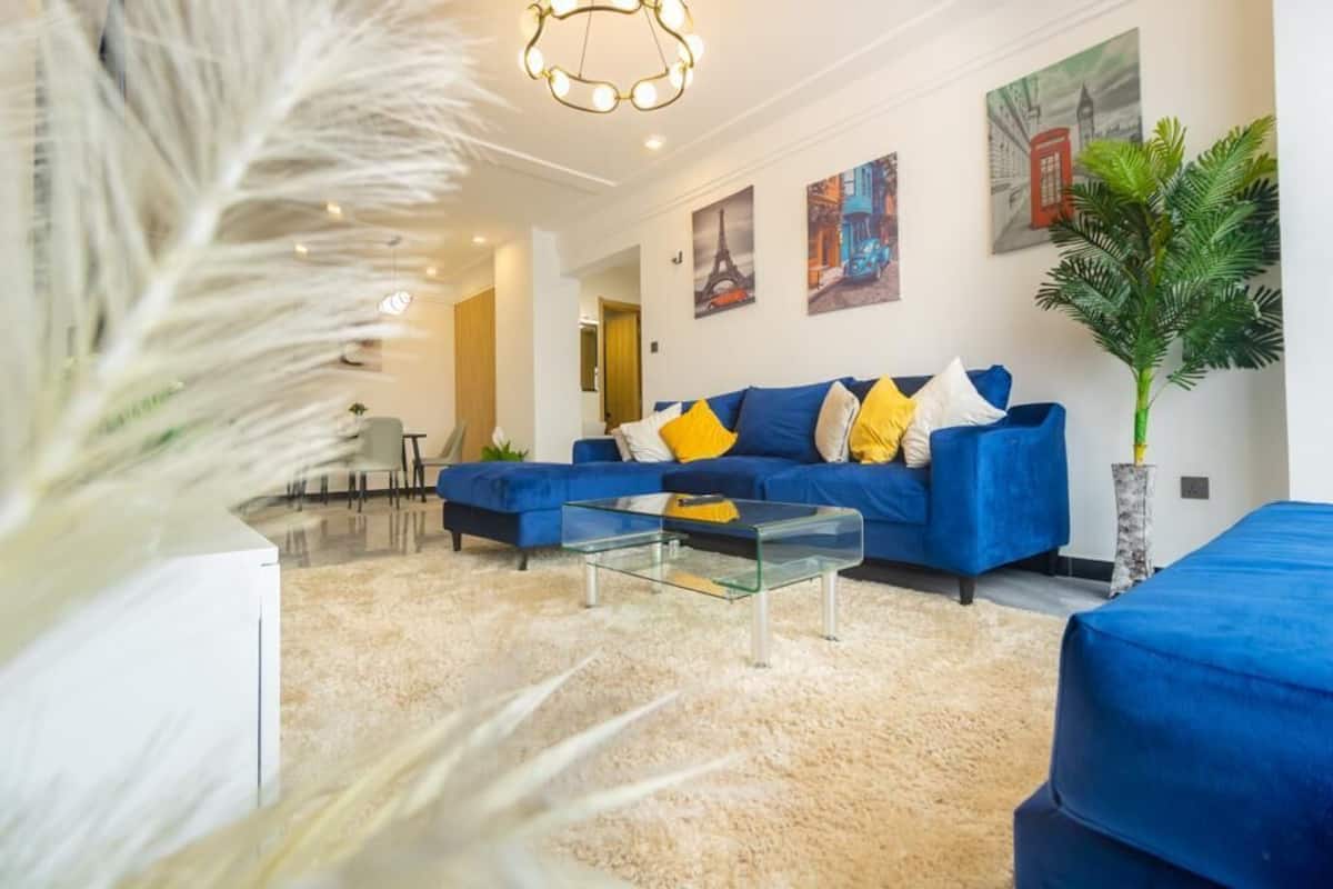 Ein modernes Wohnzimmer mit einem blauen Sofa, einem Glastisch und dekorativen Kissen.