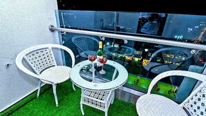 Ein Balkon mit zwei Korbstühlen und einem Glastisch, mit einer Flasche Rotwein und einem Glas.