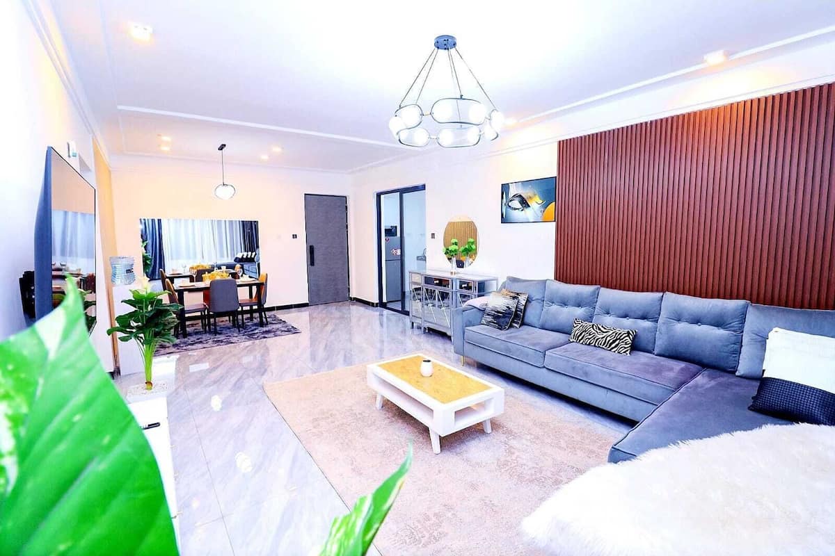 Ein modernes Wohnzimmer mit einem grauen Sofa, einem Couchtisch und einem Essbereich mit Tisch und Stühlen.