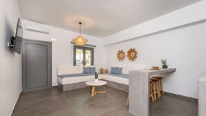 A modern living area with a sofa, a round table, and a kitchen counter. - AquaLung Suites (Santorini)