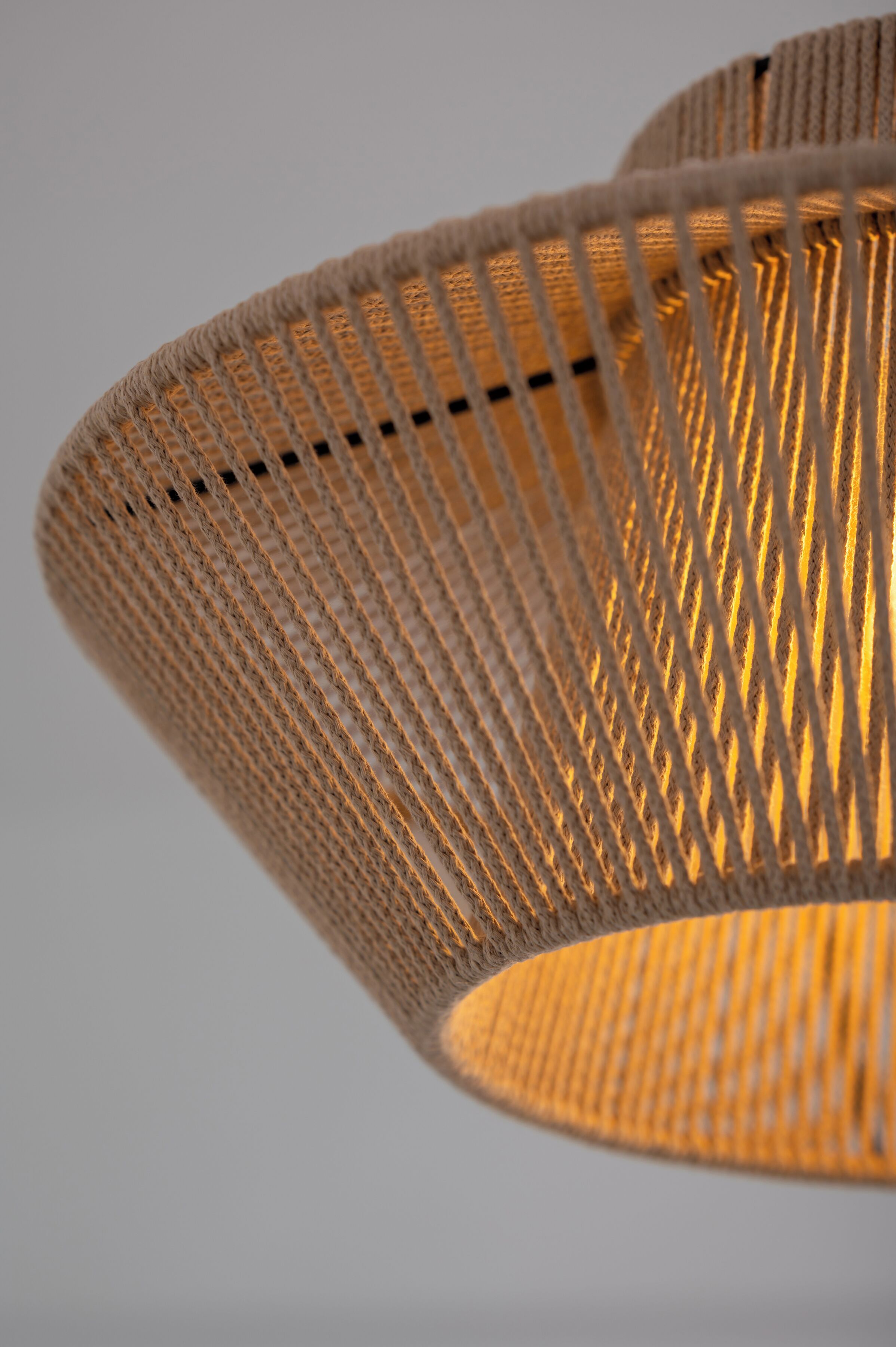 Een detailfoto van een geweven, cilindrische lamp met een warme lichtbron erin.