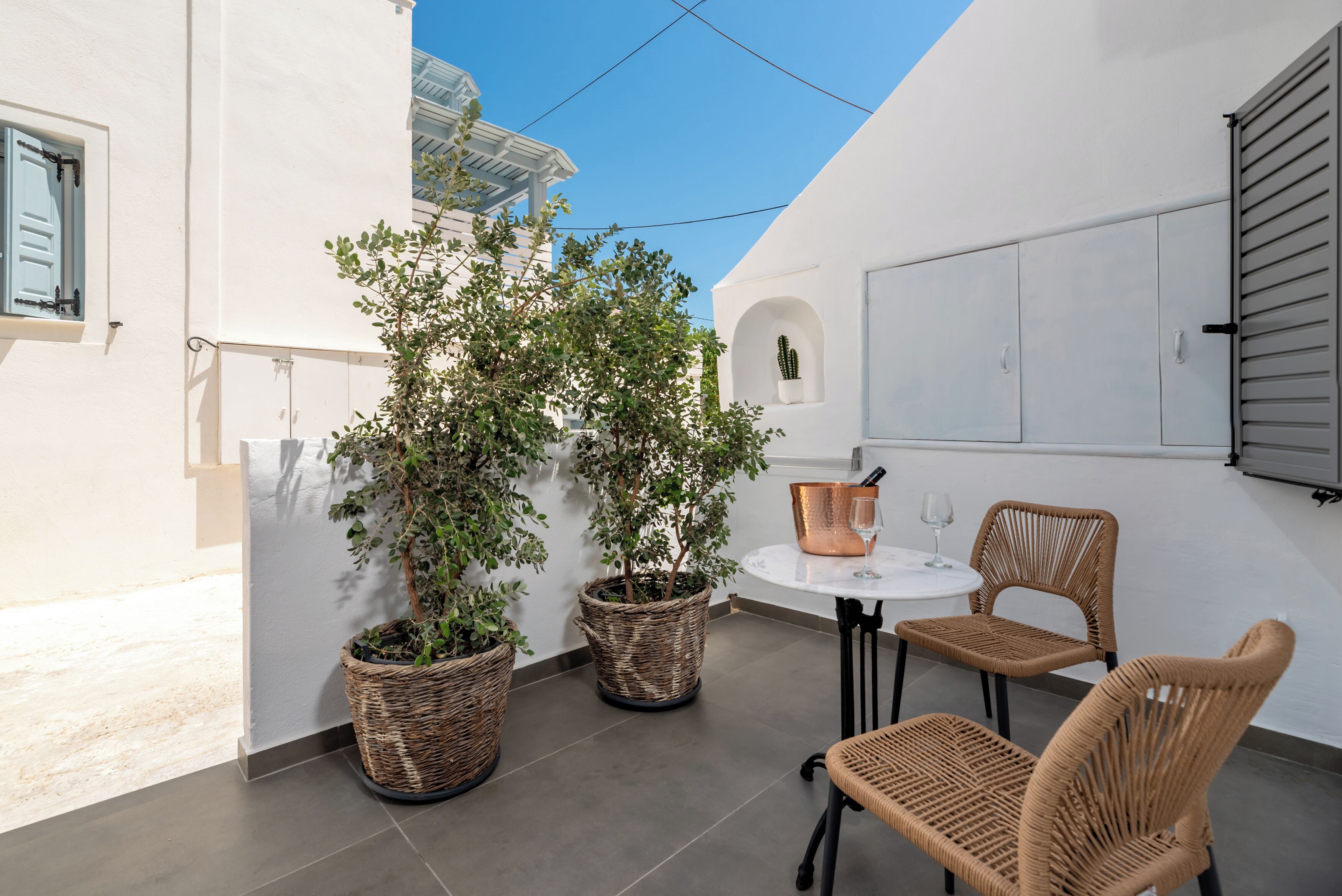 A small patio area with wicker furniture, a table, and potted plants.