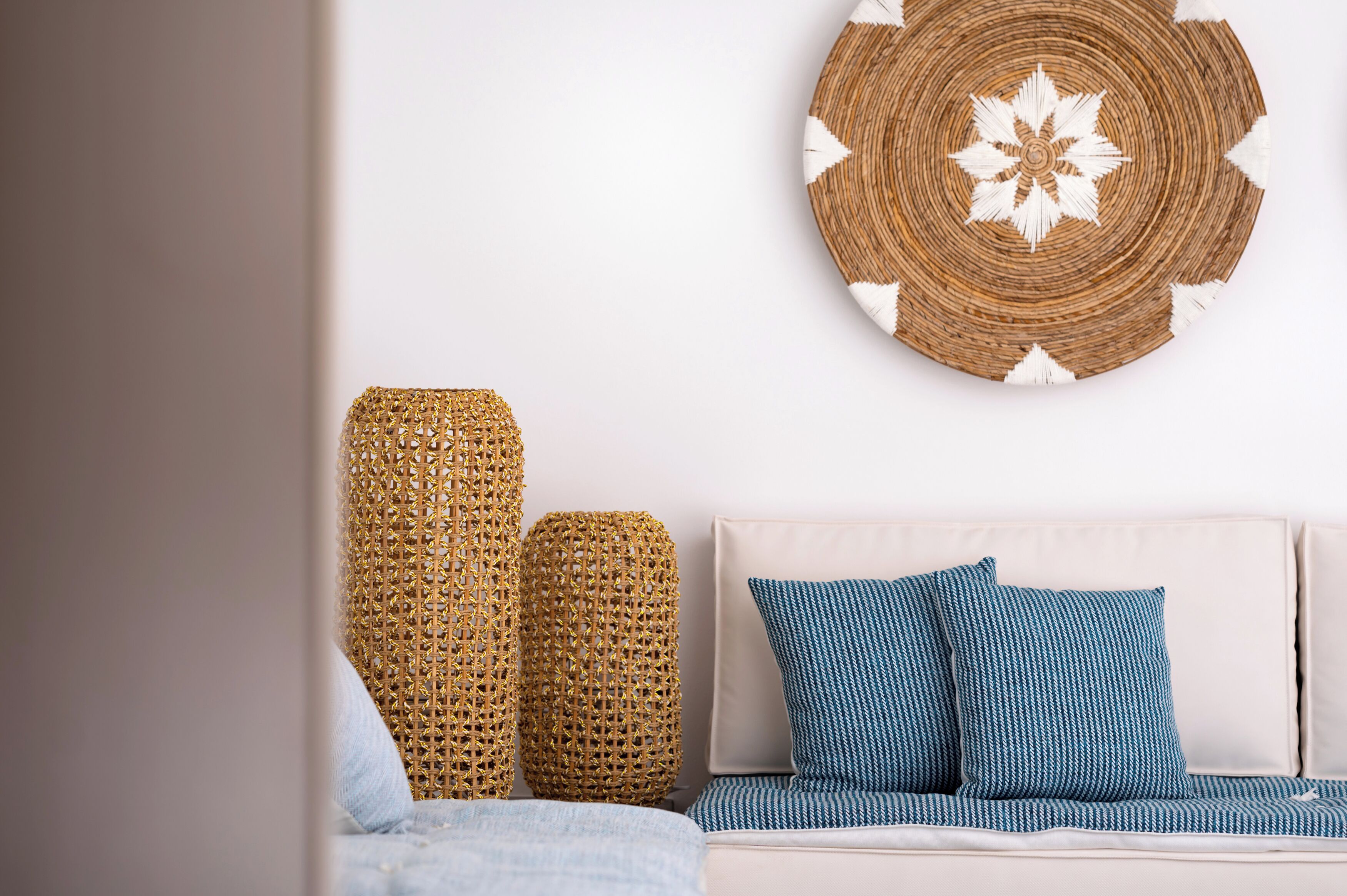 A room with a beige sofa, two blue patterned pillows, and two woven baskets on a white wall.