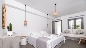 A modern bedroom with a large bed, bedside tables, a sofa, and pendant lights. - AquaLung Suites (Santorini)