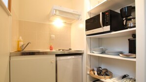 A compact kitchen with a dishwasher, microwave, and shelves with dishes and utensils. - Studio with sea view, parking, and pets allowed in La Hague (La Hague)