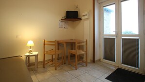 A small room with a desk, two chairs, a lamp, a shelf with a television, and a door with blinds. - Studio with sea view, parking, and pets allowed in La Hague (La Hague)