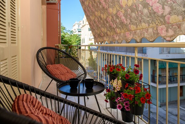 Un balcon avec des fauteuils en osier, une petite table ronde et des plantes en pot.