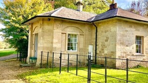 A stone building with a pitched roof, a small porch, and a fenced area in front.