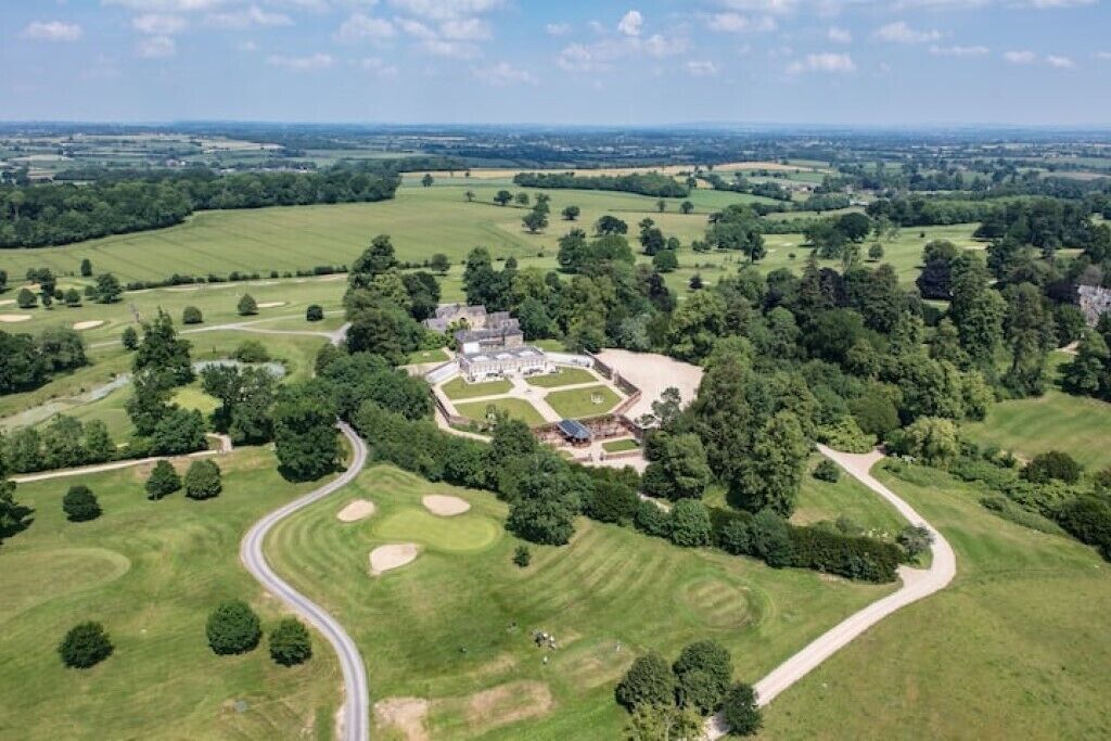 An aerial view of a golf course with a large building surrounded by lush greenery and rolling hills.