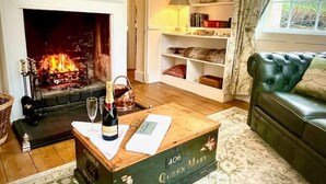 A cozy living room with a fireplace, a leather sofa, and a coffee table with a bottle and glasses.
