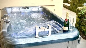 A hot tub with a bottle of champagne and a glass on the edge.