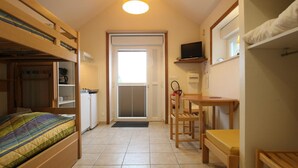 A compact room with a bunk bed, a small kitchenette, a desk with a chair, and a television on the wall. - Unique studio in La Hague, PMR access, pets allowed and WiFi (La Hague)