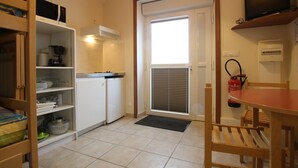 A compact kitchen with a microwave, stove, and refrigerator. There is a dining table with chairs and a fire extinguisher on the wall. - Unique studio in La Hague, PMR access, pets allowed and WiFi (La Hague)