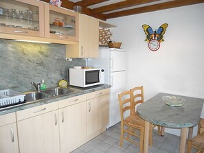 Uma cozinha com armários de madeira, micro-ondas, geladeira, pia e uma mesa de jantar com cadeiras.