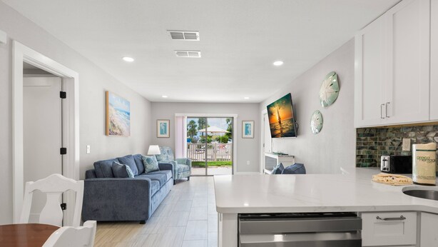 A modern kitchen with white cabinetry, a central island, and a dining area with a wooden table and white chairs.