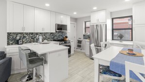 A modern kitchen with white cabinets, a central island, a microwave, a refrigerator, and a dining area with a table and chairs.