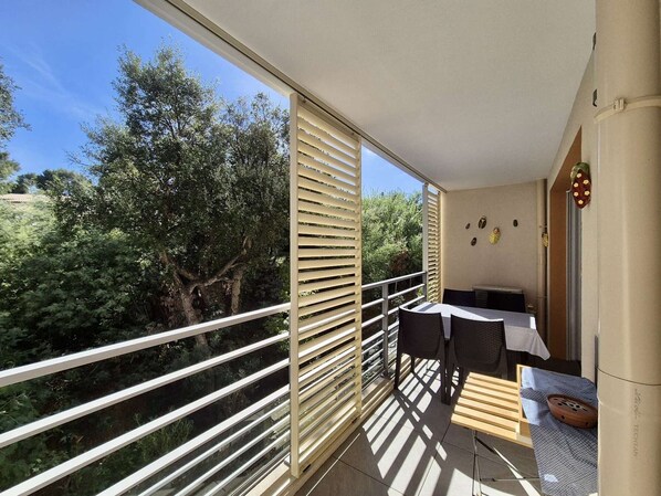 A balcony with a table and chairs, a view of trees, and a wall with decorative items.