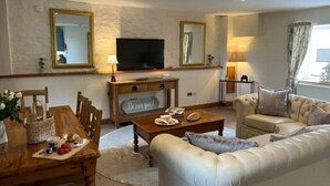 A living room with a wooden dining table, a sofa, a television, and a mirror. - The Bell Tower, Orchardleigh Estate (Frome)