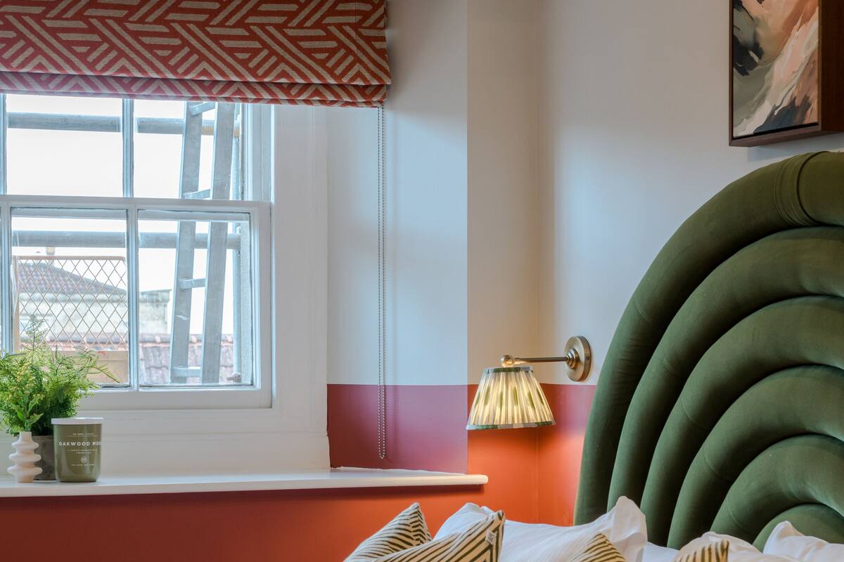 Un dormitorio con cama, almohadas estampadas, ventana con vistas, lámpara de pared y lámpara del techo.