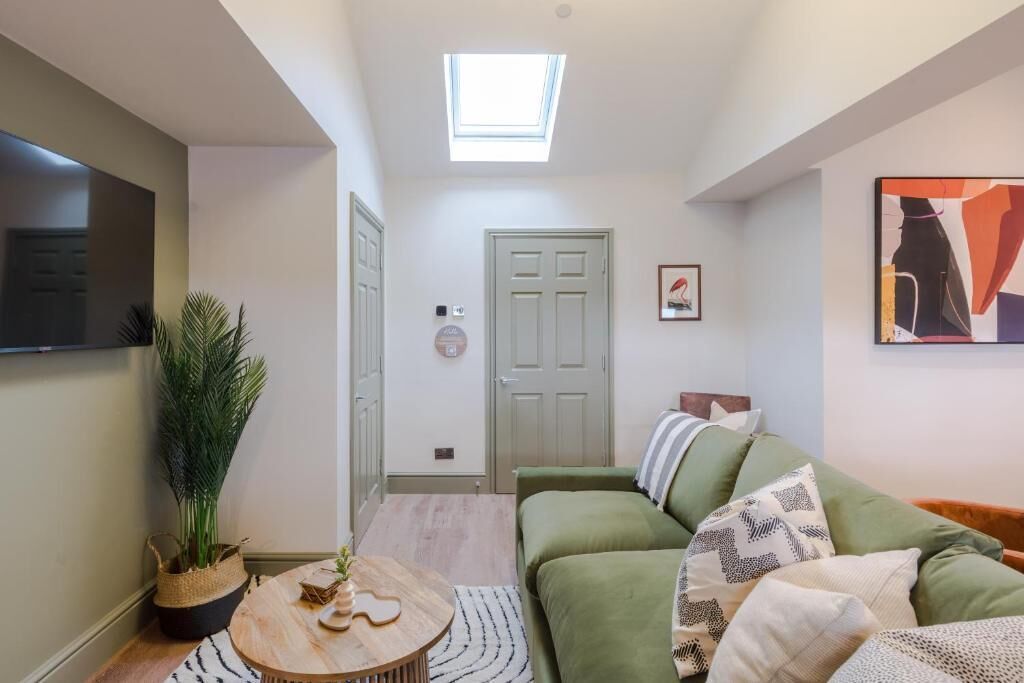A modern living room with a green sofa, a round wooden coffee table, a potted plant, and a skylight above a door.
