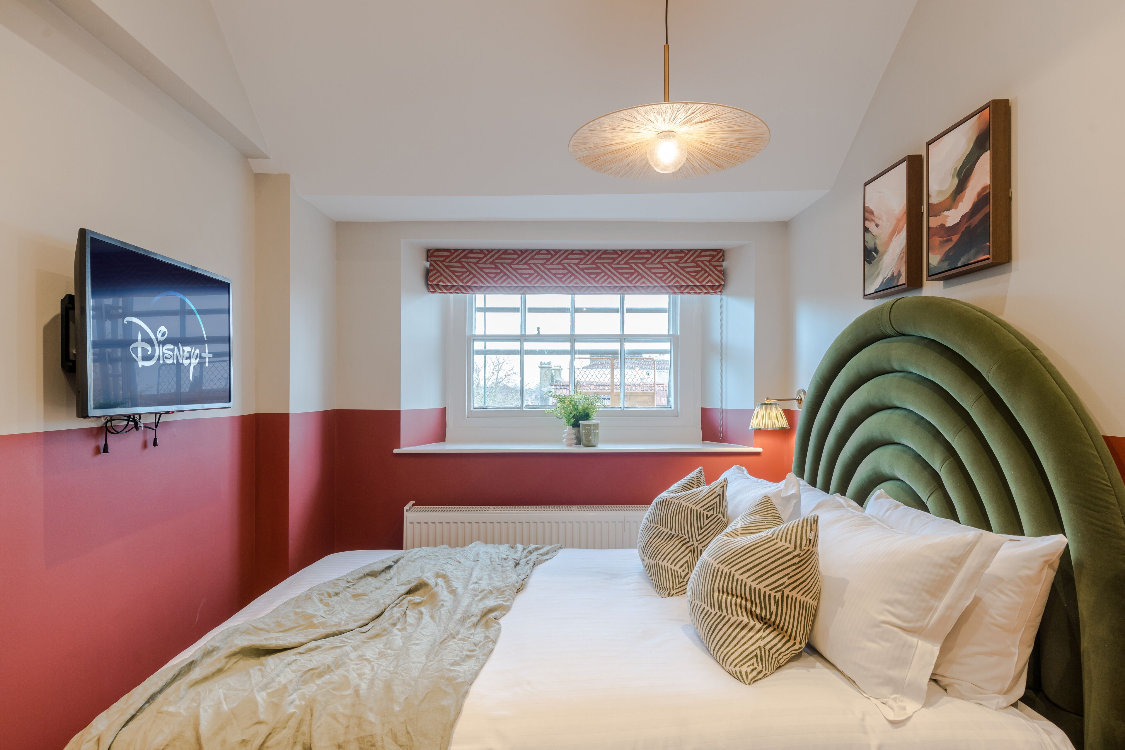 A bedroom with a bed, a television, a window with a view, and a green headboard.