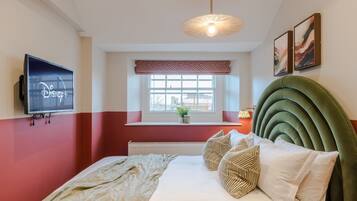 A bedroom with a bed, a television, a window with a view, and a green headboard.