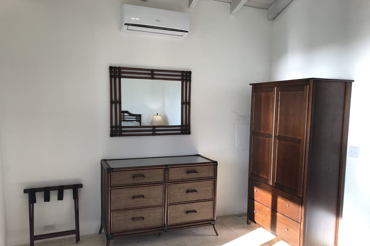 Una habitación con un armario de madera grande, un tocador de mimbre, una mesita y un espejo en la pared.