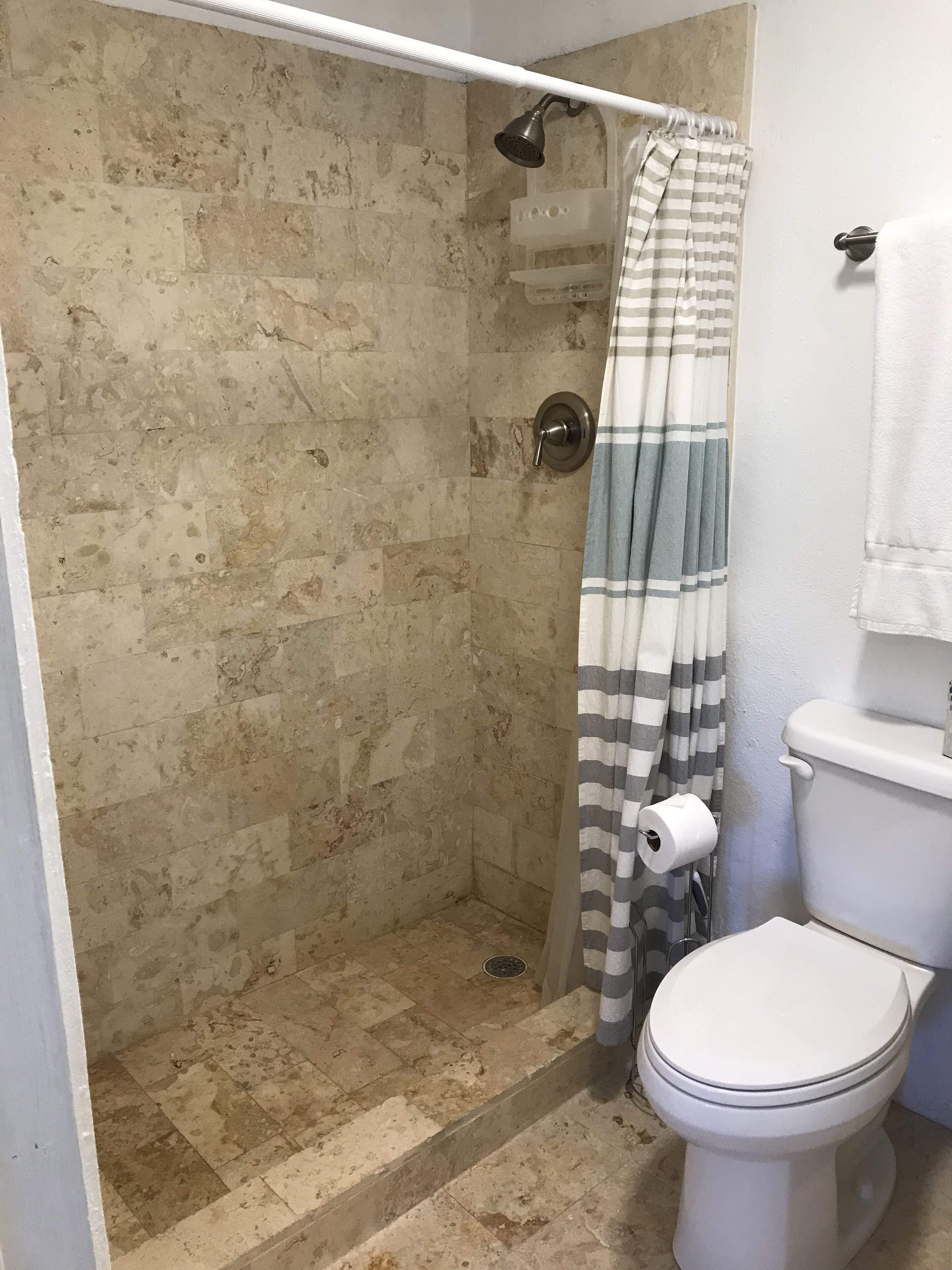 Un baño con ducha, inodoro y toallero.