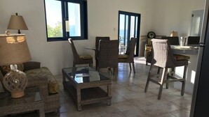 Un espacio habitable amplio con muebles de mimbre, una mesa de centro de vidrio y vistas al exterior a través de grandes ventanales.