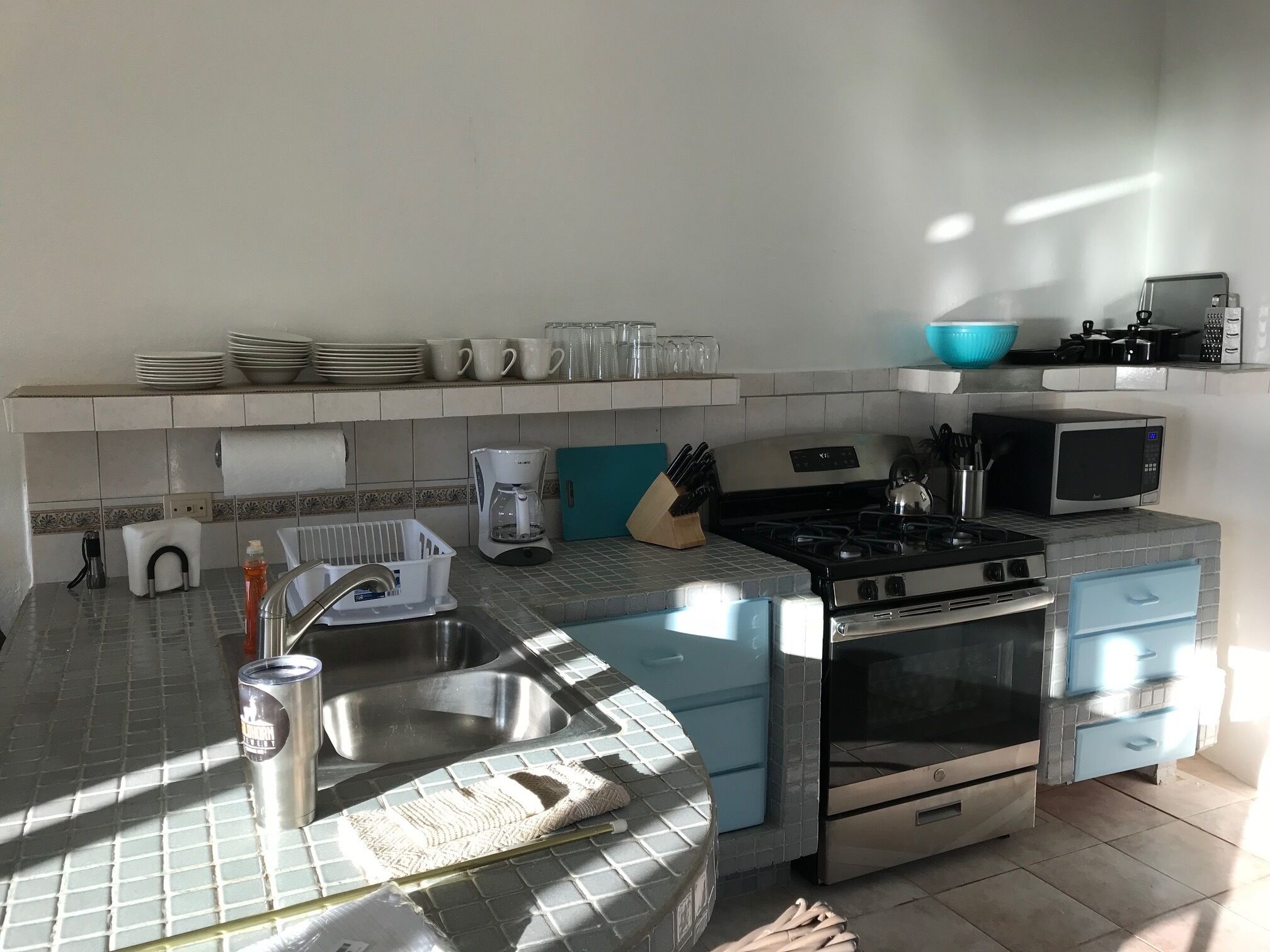 Una cocina con fregadero, estufa, microondas y diversos utensilios.