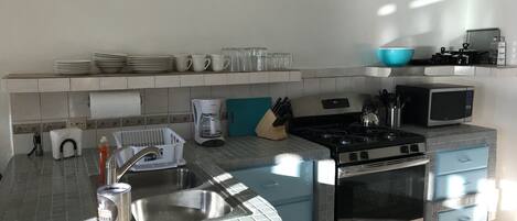 Una cocina con fregadero, estufa, microondas y diversos utensilios.