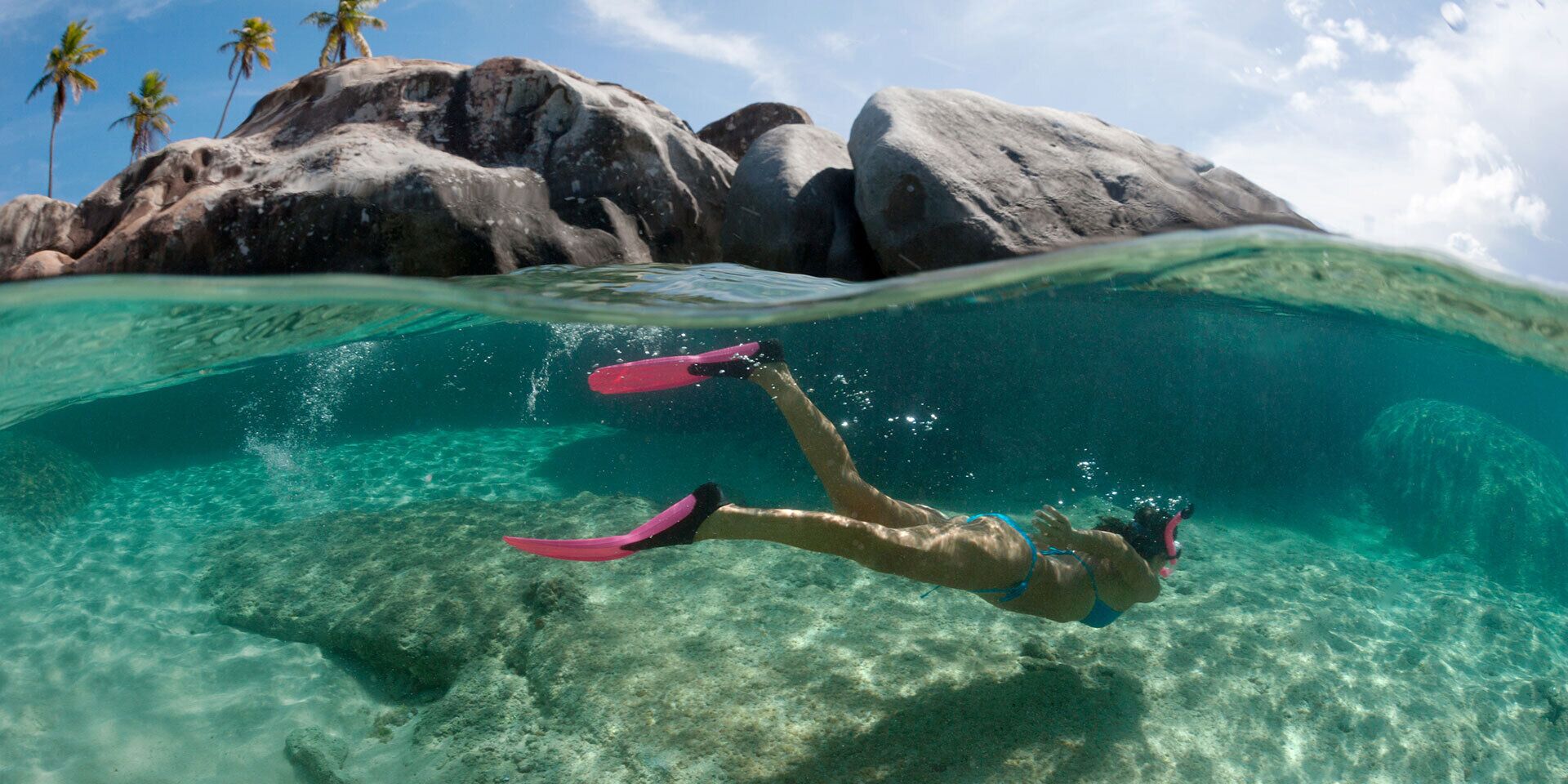 A person snorkeling underwater with clear water and rocks.
