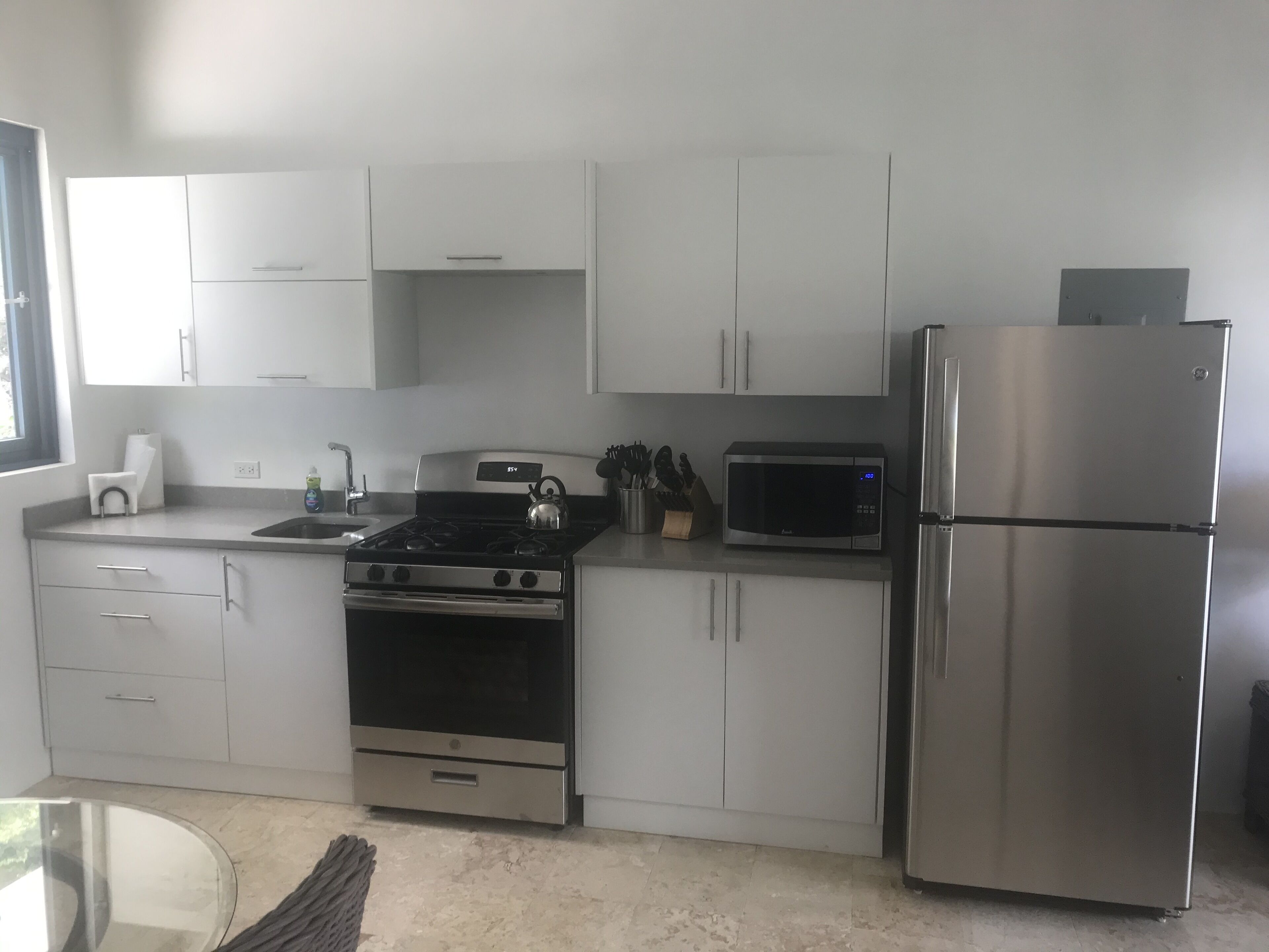 Una cocina moderna con armarios blancos, un refrigerador de acero inoxidable, un microondas, una estufa y un lavaplatos.