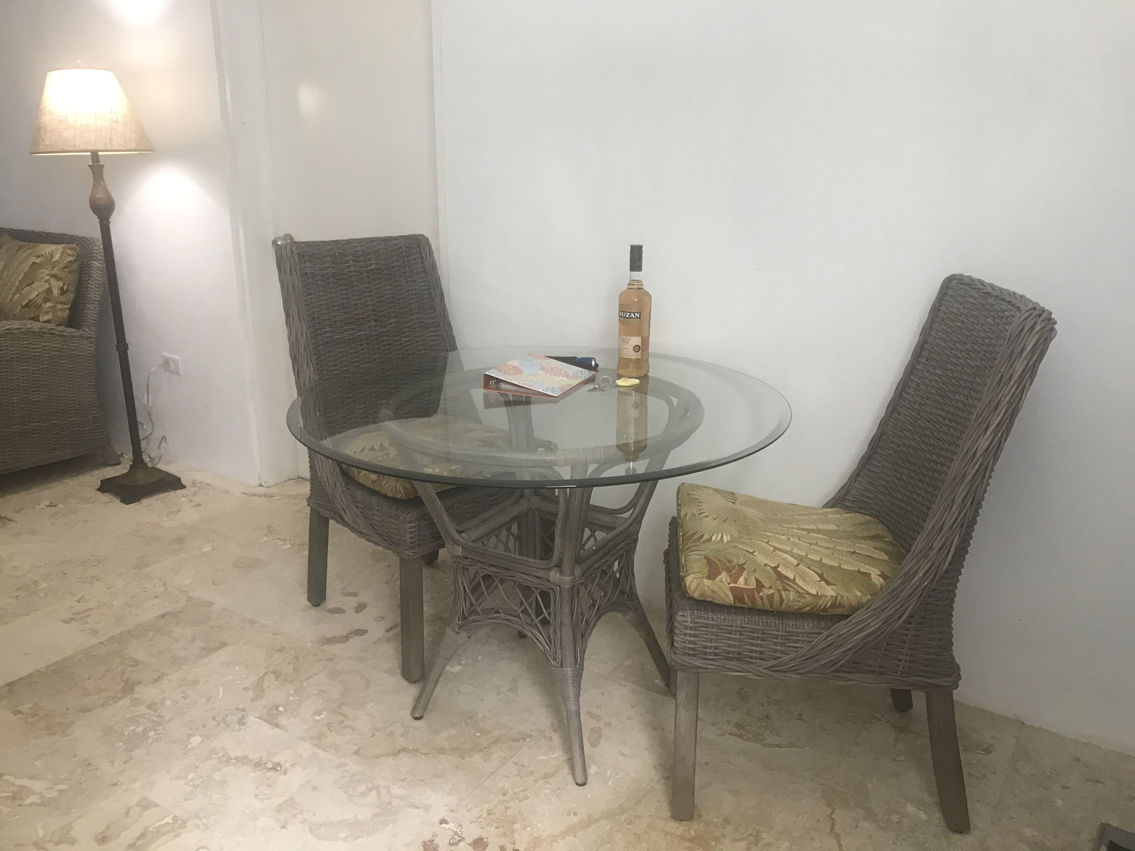 Una mesa redonda de vidrio con sillas de mimbre, una botella y un libro encima.