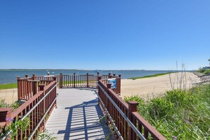 Una passerella in legno che conduce a una spiaggia, con vista limpida sull'acqua e sulla costa lontana.