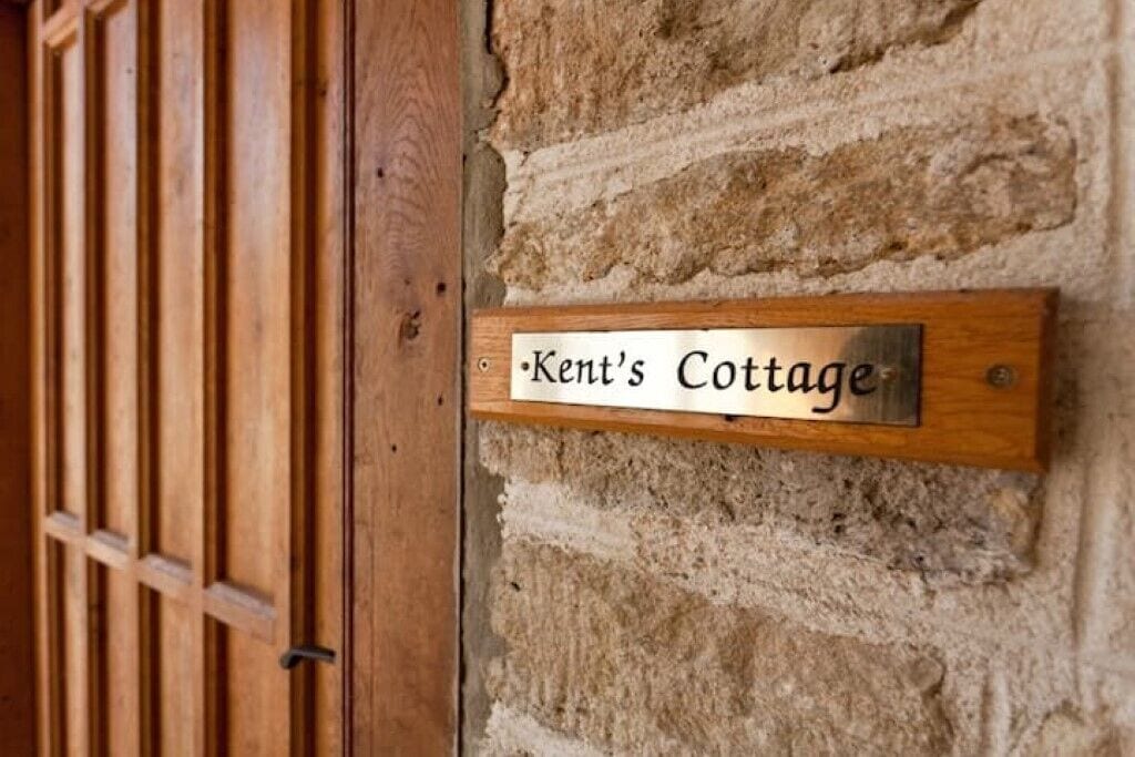 A wooden sign with the text "Kent's Cottage" mounted on a stone wall.