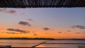 Une terrasse offrant une vue sur un coucher de soleil se reflétant sur une étendue d’eau, avec une balustrade et un ciel dégagé.