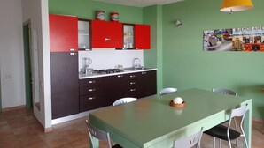 Une cuisine compacte avec des meubles de rangement rouges et noirs, une table à manger verte et un luminaire suspendu jaune.