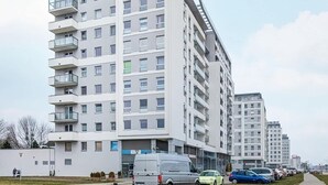 A modern apartment building with multiple floors, a paved walkway, and parked cars. - Spacious Apartment | Two Bedrooms and Terrace (Gdańsk)