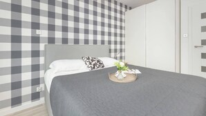 A neatly arranged bedroom with a checkered wall pattern, a bed with white and patterned pillows, and a bedside table with a vase and glasses. - Spacious Apartment | Two Bedrooms and Terrace (Gdańsk)