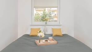 Un lit bien fait, avec un plateau contenant un beignet et une tasse, deux oreillers et un vase rempli de fleurs.