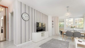 Un salon moderne avec un mur à rayures, un téléviseur à écran plat, un coin repas comprenant une table et des chaises, et un lustre.