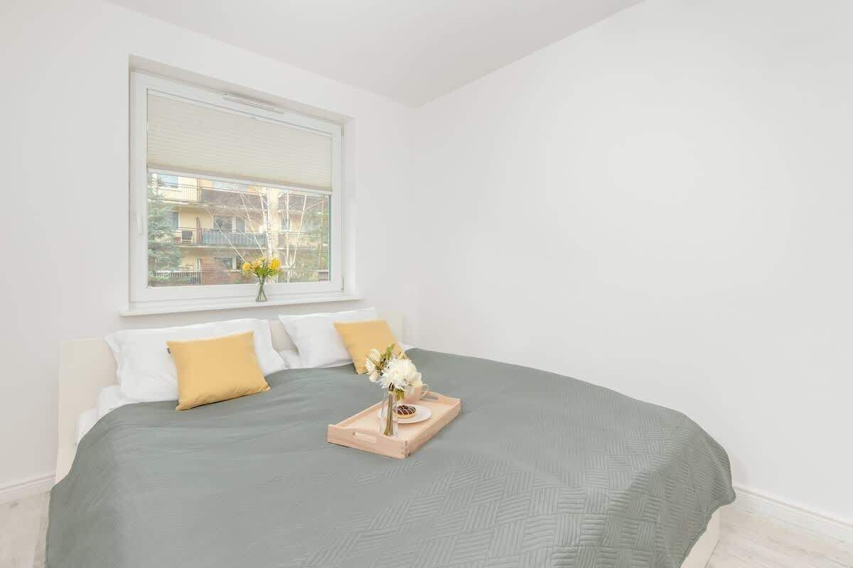 A neatly made bed with a grey bedspread, two pillows, and a tray with flowers and a plate.