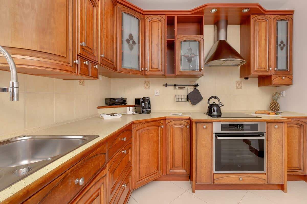 A kitchen with wooden cabinets, a stainless steel sink, a built-in oven, and a kettle.
