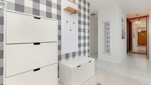 Une chambre d’hôtel avec un motif à carreaux sur le mur, une armoire blanche, un petit meuble blanc et une étagère en bois.