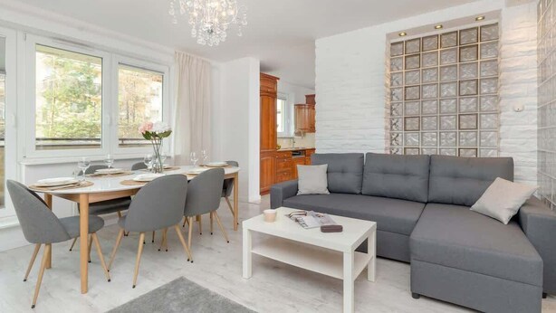 Un salon moderne avec un canapé d’angle gris, une table à manger avec des chaises et un lustre.