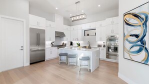A modern kitchen with white cabinetry, stainless steel appliances, a central island with bar stools, and recessed ceiling lighting. - 560 Perfectly Situated · Walk 2 Beaches & The Ritz (Naples)