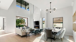A modern living room with a fireplace, a dining area, and large windows. - 560 Perfectly Situated · Walk 2 Beaches & The Ritz (Naples)