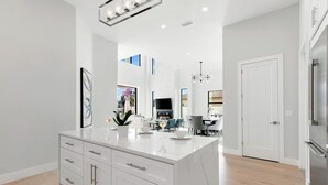 A modern kitchen with white cabinetry, a marble island, and a dining area with a chandelier. - 560 Perfectly Situated · Walk 2 Beaches & The Ritz (Naples)